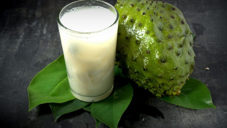 Um copo de suco de graviola com folhas frescas de graviola no fundo de madeira cinza