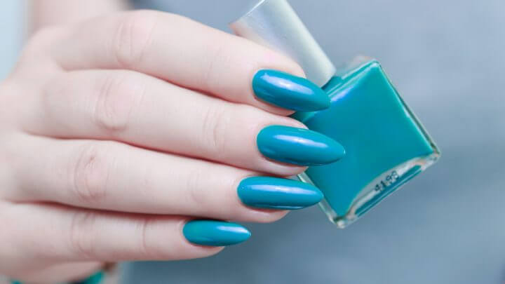 Mãos femininas com unhas na cor azul segurando um esmalte azul