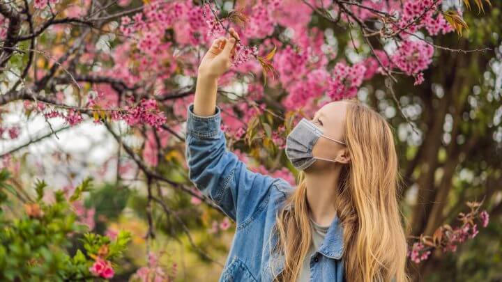 Mulher usando máscara e olhando uma árvore com flores rosas