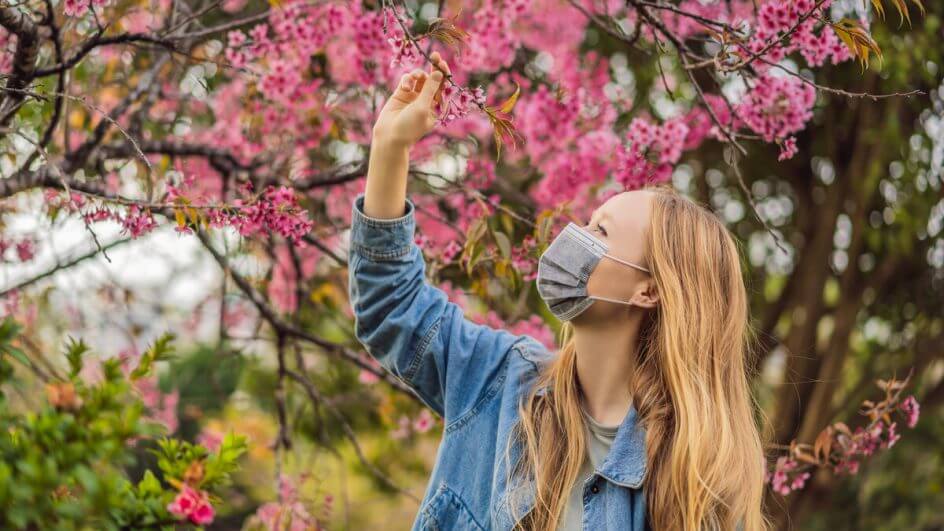Mulher usando máscara e olhando uma árvore com flores rosas