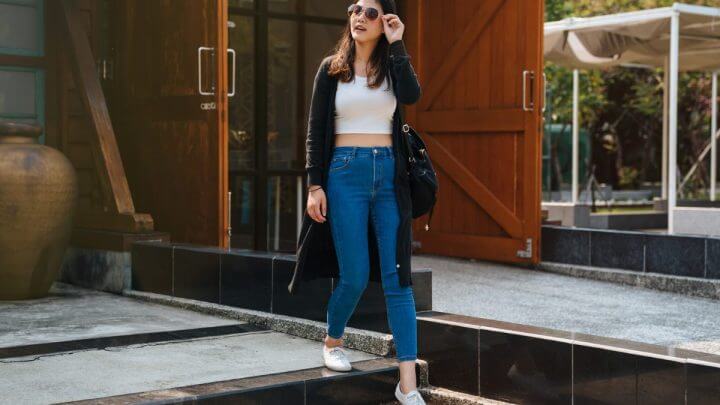 Mulher usando blusa branca, calça jeans e óculos de sol andando na rua
