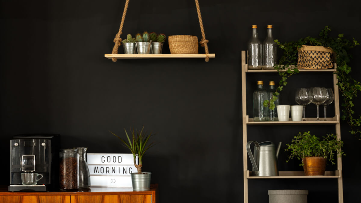 Balcão com máquina de café e potes com grãos de café. Ao lado, estante com itens de cozinha