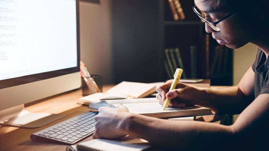 Jovem estudando, com livros e computador ligado