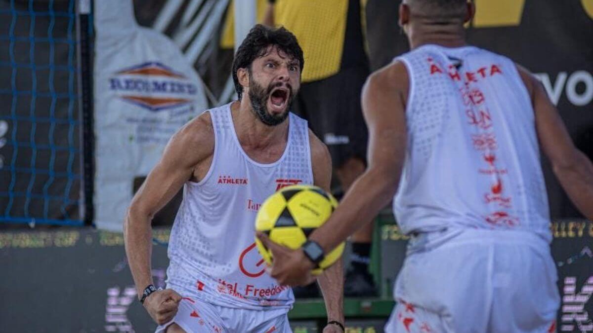 Imagem mostra Juninho SC com regata branca e uma pessoa de costas também vestido de branco e segurando uma bola