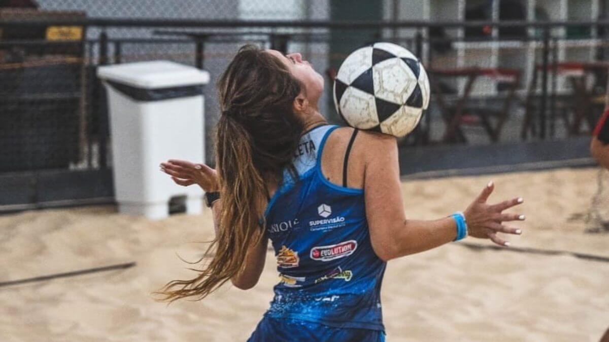 Imagem mostra mulher vestindo uma regata azul de costas e dominando uma bola no ombro