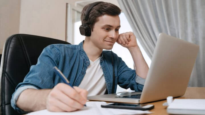 Menino sorrindo usando fone de ouvido estudando em um notebook