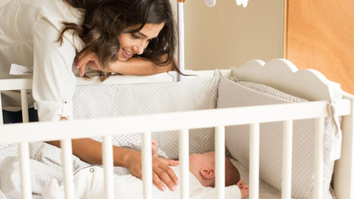Mãe apoiada no berço olhando o bebê dormir