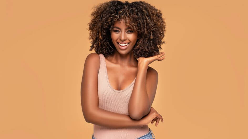 Mulher com mão no cabelo cacheado. Ela está em fundo laranja