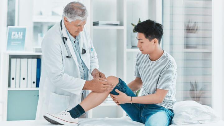 Médico examinando joelho de jovem dentado em maca