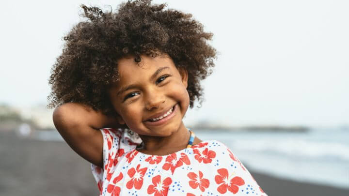 Menina sorrindo de cabelo cacheado solto e com a mão atrás da cabeça