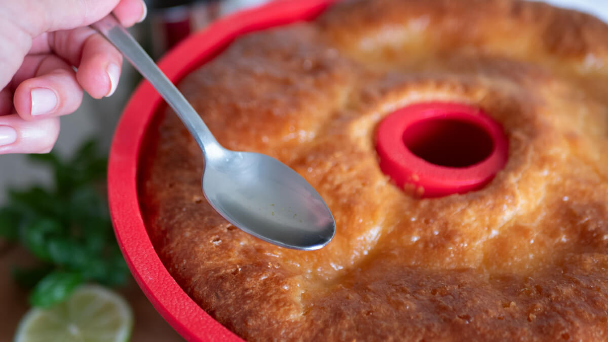 Mão feminina segurando colher com calda em cima de bolo