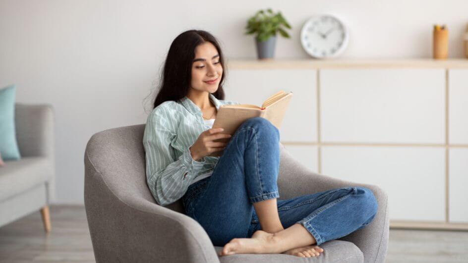 Mulher sentada confortavelmente em poltrona lendo livro