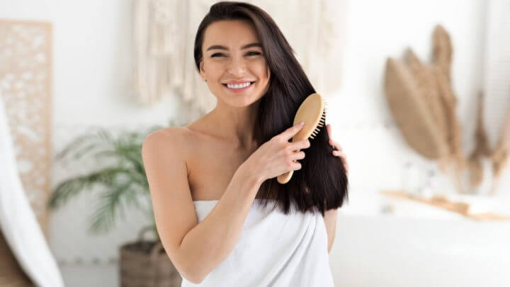 Mulher com toalha branca sorrindo e penteando os cabelos