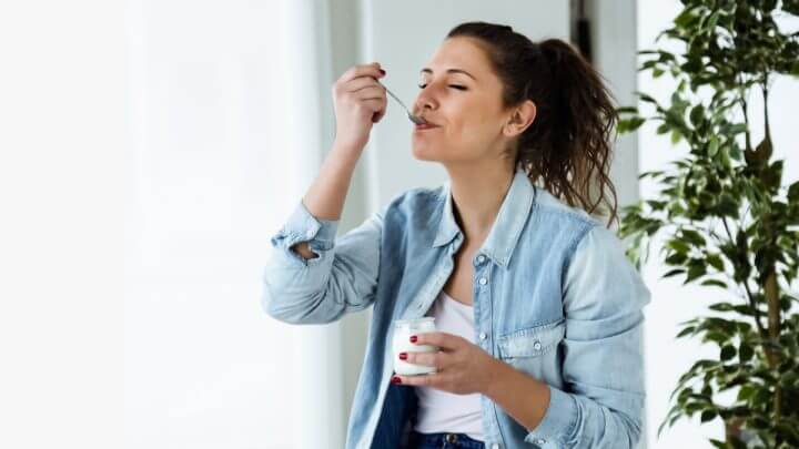 Mulher com blusa branca e jaqueta jeans comendo iogurte
