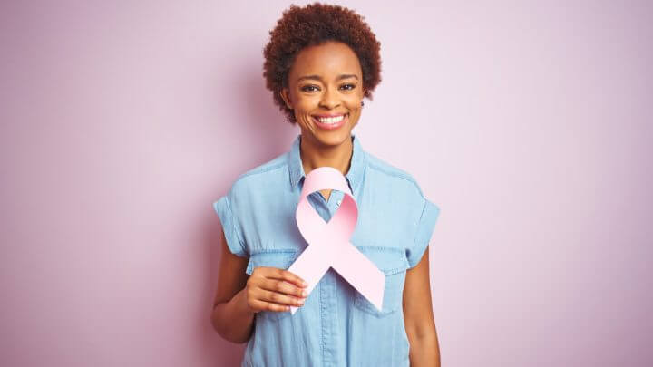 Mulher de macacão azul segurando um laço rosa em frente ao peito