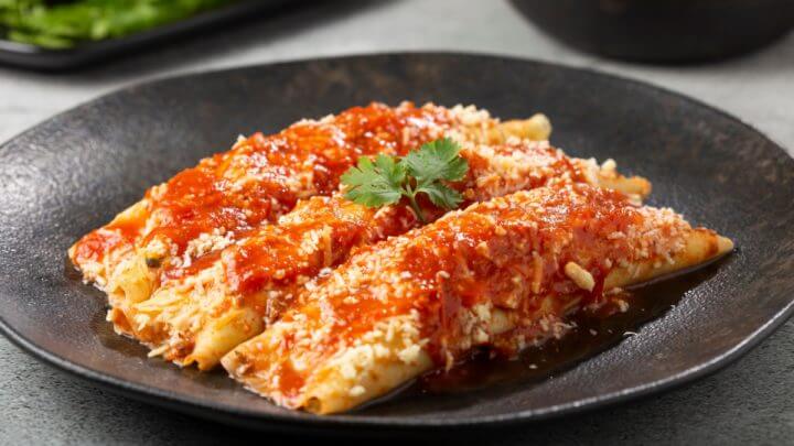 Três panquecas, uma ao lado da outra, com molho de tomate e queijo em cima de prato preto