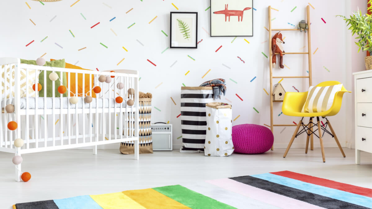 Quarto de bebê com cadeira amarela, berço branco, tapete e decorações muito coloridas.