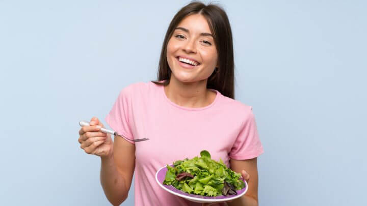 Mulher sorrindo segurando um prato com salada