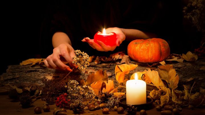 Mãos femininas mexendo em plantas em uma mesa com velas e abóbora