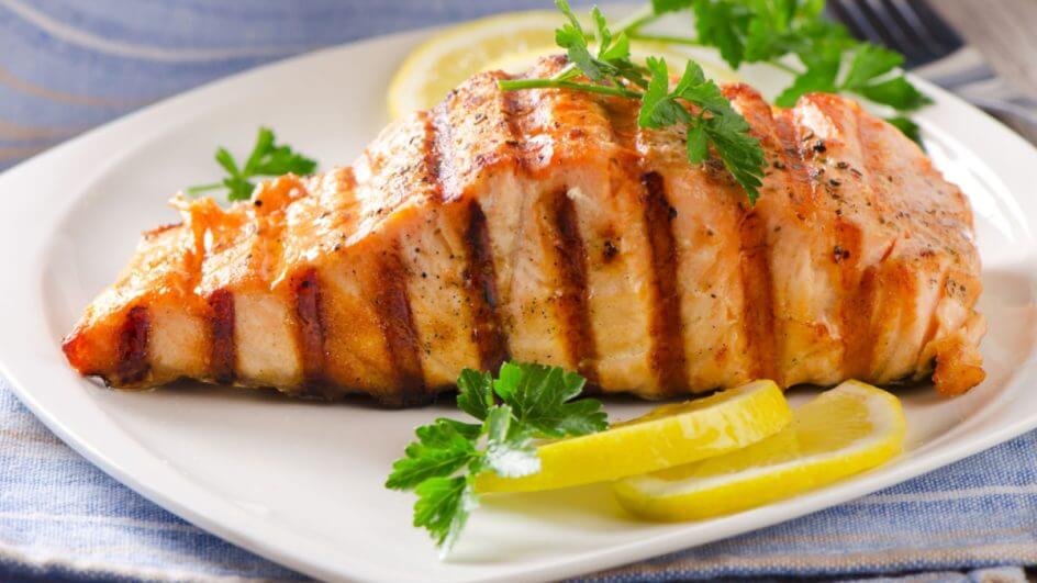 Prato branco com salmão grelhado, salsinha e fatias de limão