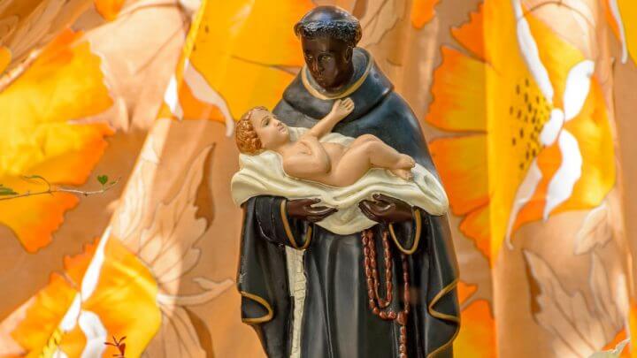 Estátua de São Benedito segurando menino Jesus nos braços e em fundo amarelo