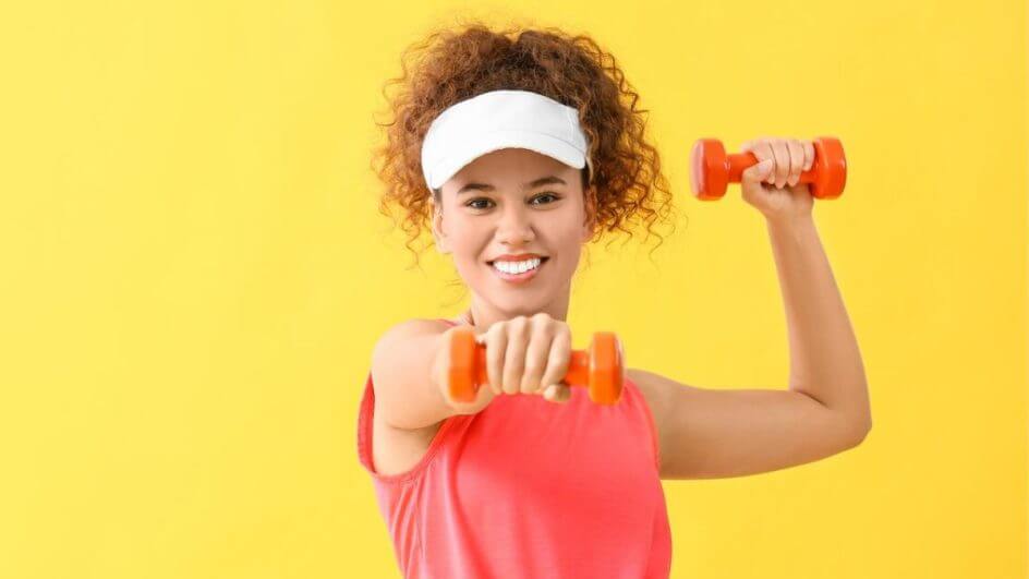 Menina usando boné branco e blusa rosa segurando um peso de academia rosa