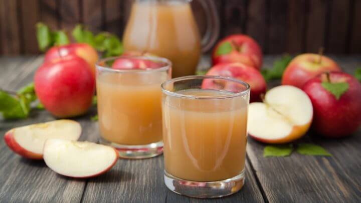Dois copos com suco de maçã em cima de uma mesa de madeira