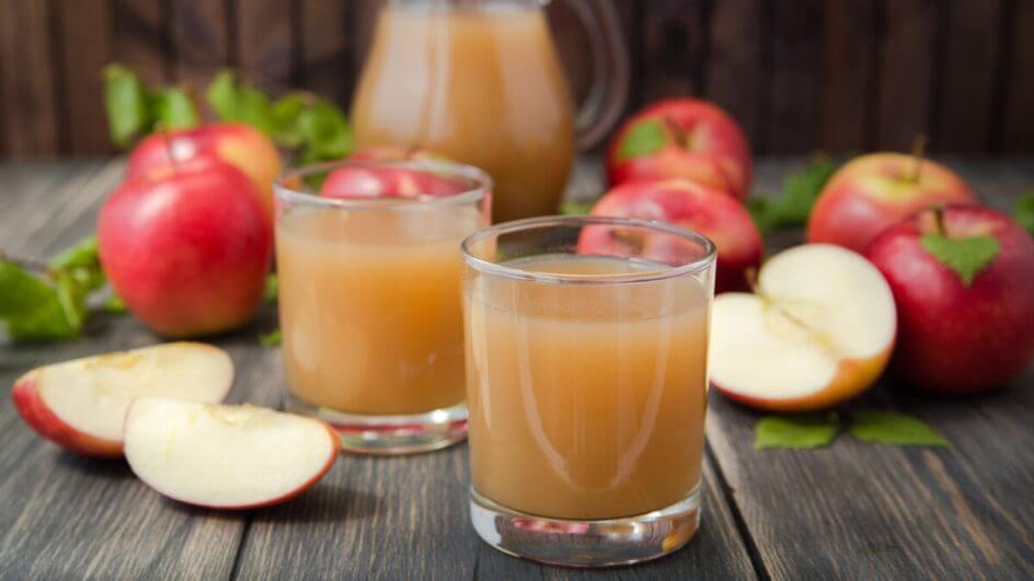 Dois copos com suco de maçã em cima de uma mesa de madeira