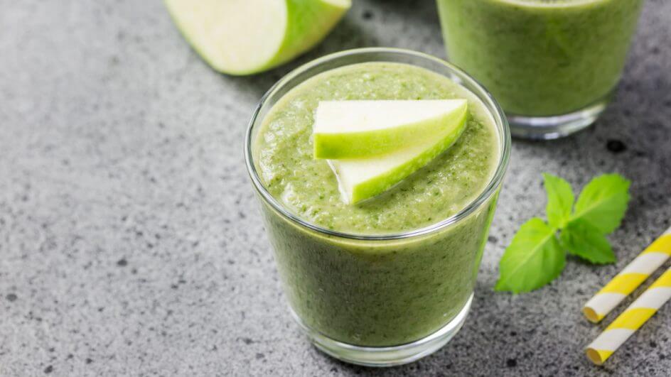 Copo de vidro com suco verde e pedaços de maçã-verde em cima
