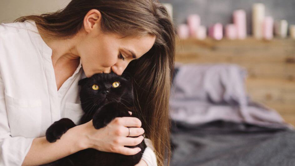 Mulher dando um beijo na cabeça de um gato preto