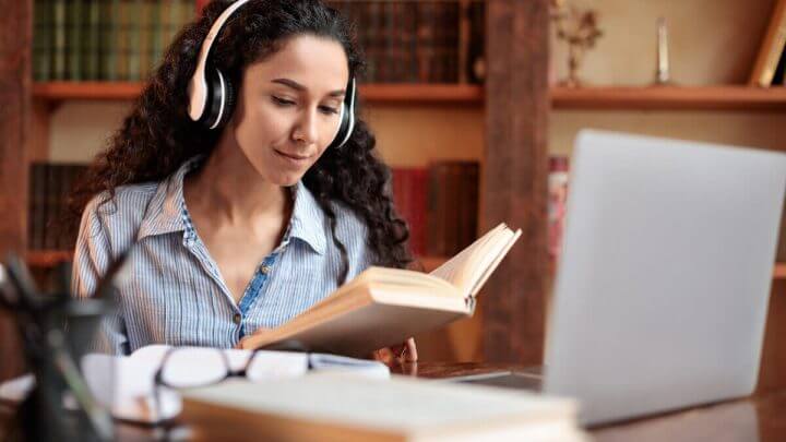 Mulher sentada usando fone e segurando um livro