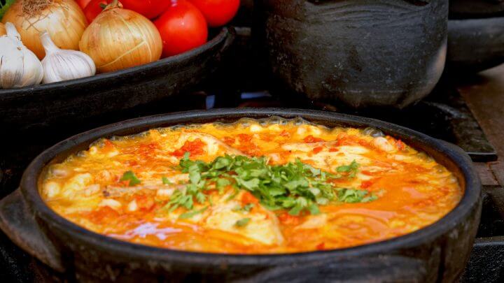 Panela preta com moqueca polvilhada com cheiro-verde