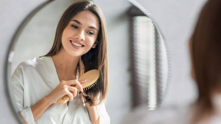 Mulher penteando seu cabelo com escova em frente ao espelho no banheiro
