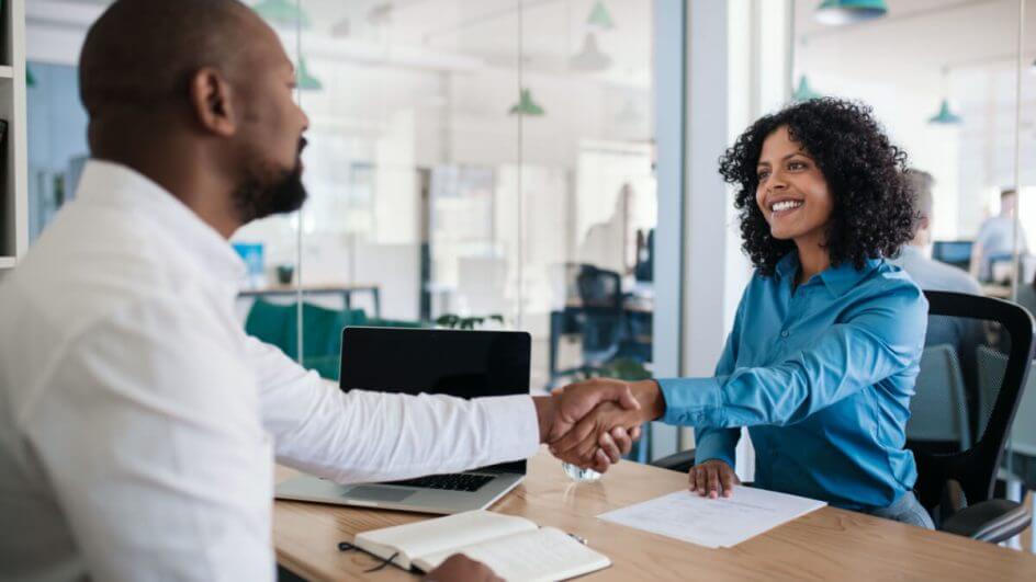 Homem e mulher sentados à mesa se cumprimentando