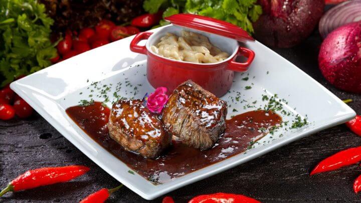 Dois pedaços de carne em um prato branco com molho marrom