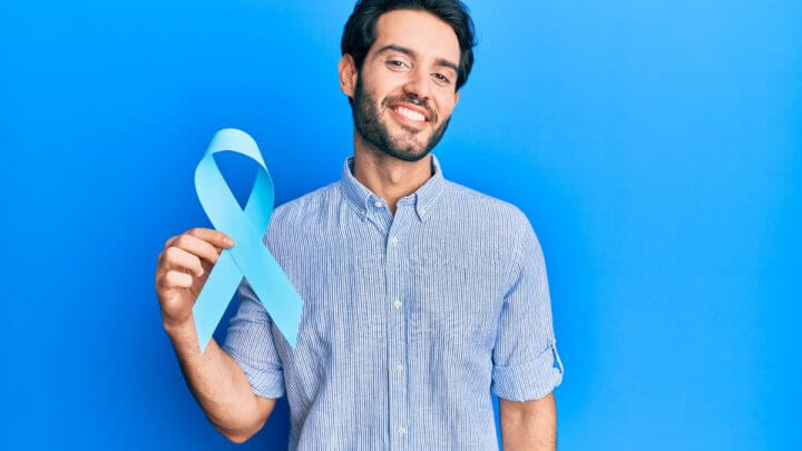 Homem de camisa azul segurando laço azul. Ele está em fundo azul