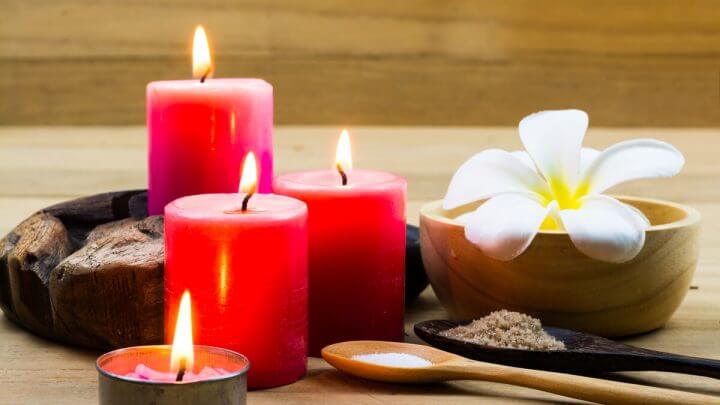 Três velas vermelhas, flor branca e colher de pau em cima de uma mesa de madeira