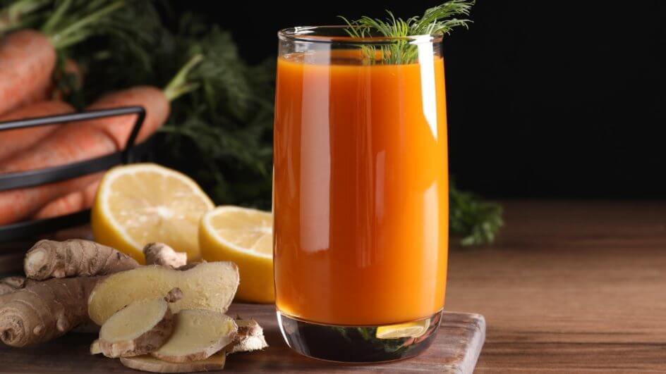 Copo de vidro com suco de laranja, gengibre e cenoura em cima de uma mesa de madeira