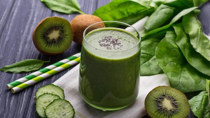 Copo de vidro com suco verde e semente de chia. Kiwi, espinafre e pepino em volta do copo