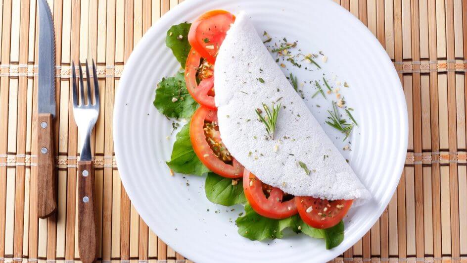 Tapioca com tomate e rúcula em cima de um prato branco