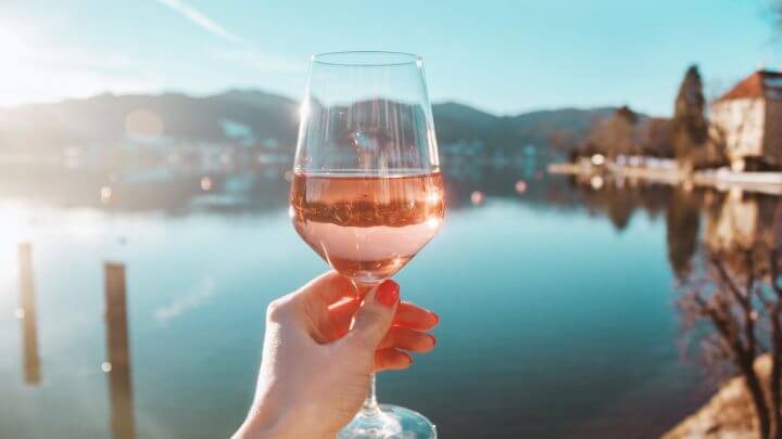 Mão feminina segurando taça de vinho rosé na na costa do lago Tegernsee