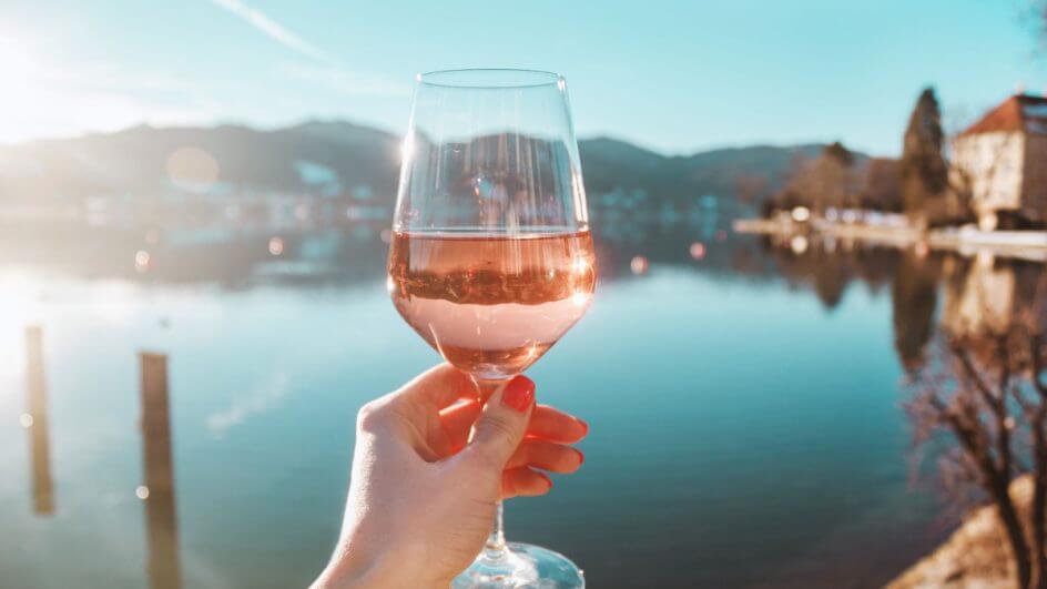 Mão feminina segurando taça de vinho rosé na na costa do lago Tegernsee