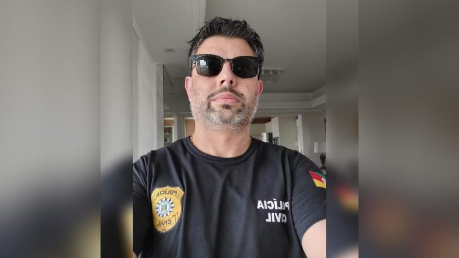 Homem branco de cabelo e barba grisalho, com óculos escuro e camisa da Polícia Civil