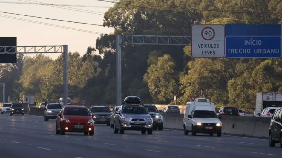 Imagem de uma rodovia com carros circulando com os faróis acesos durante o dia