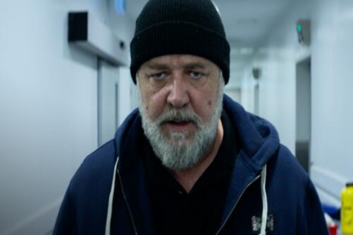 Cena do filme "A Teia"; homem barbudo com casaco azul