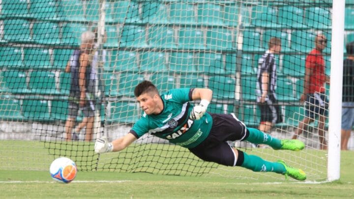 Tiago Volpi aparece pulando para defender e vestido com uma camisa verde e com o símbolo do Figueirense no meio