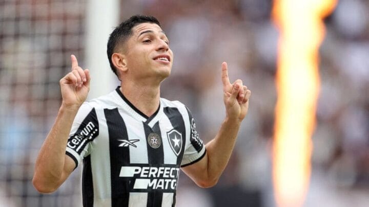 Imagem mostra Savarino celebrando e com a camisa listrada em preto e branco do Botafogo