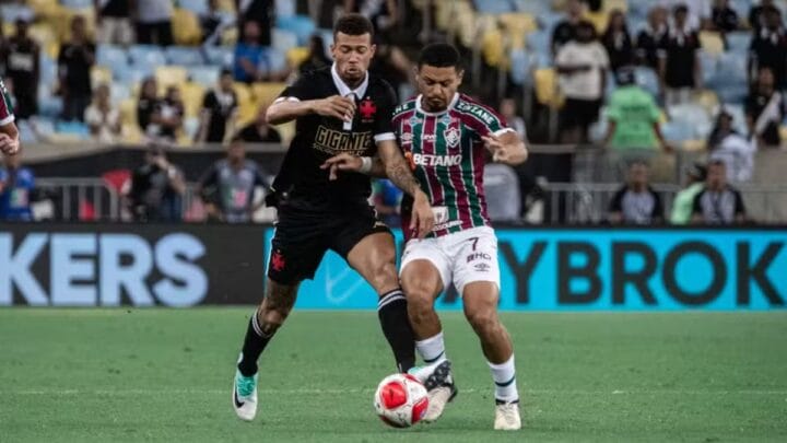 Imagem mostra um jogador do Vasco com a camisa preta e um do Fluminense com a camisa listrada em verde e vermelho