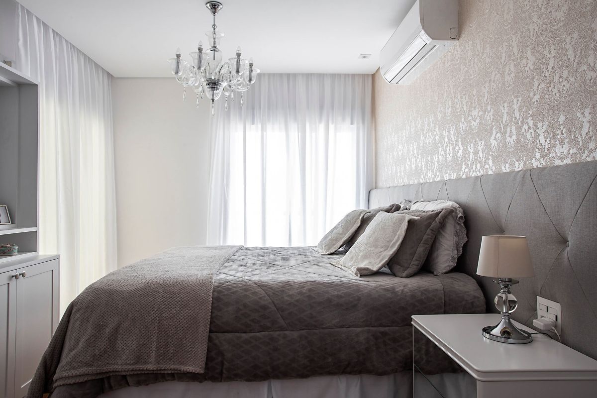 Cabeceira com integração estofada marrom em um quarto com papel de parede marrom, lustre e cortinas brancas