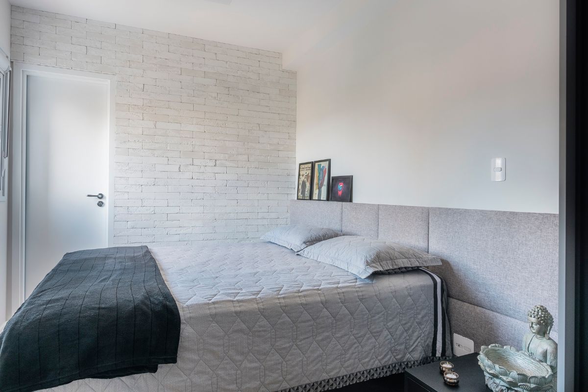 Cabeceira com estofado cinza atrás de uma cama com lençol cinza e manta verde